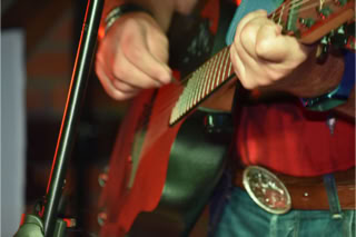 Person spielt Gitarre, Nahaufnahme der Hände und des Instruments, mit Mikrofon im Vordergrund.