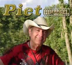 Mann mit Cowboyhut und rotem T-Shirt lächelt in die Kamera, im Hintergrund Bäume und blauer Himmel, Text "Piet" oben links.